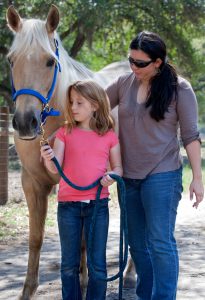 Instructor teaching a young girl how to walk a horse.